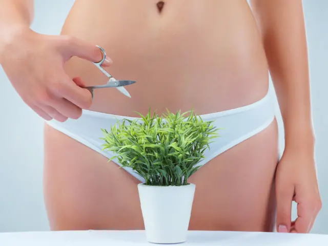 Una mujer en ropa interior frente a una planta que cubre su entrepierna sostiene unas tijeras.