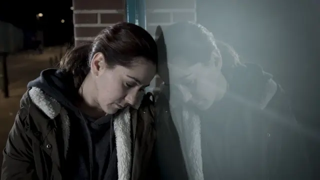 mujer apoya su rostro en una ventana con visible pesadumbre.