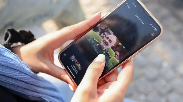 Manikürlü bir kadın eli cep telefonu tutuyor, ekranda Hüseyin Selami'nin fotoğrafı var