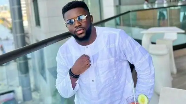 Mama Deola to wọ asọ funfun toketilẹ, o fi igo soju, joko lori aga kan, awọn aga ijoko yii ka.