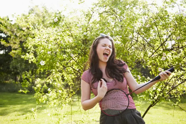 A woman singing with a racquet as a guitar
