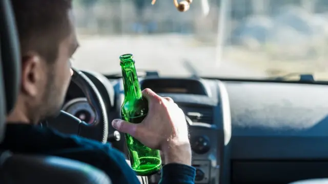Hombre manejando con una cerveza en la mano.
