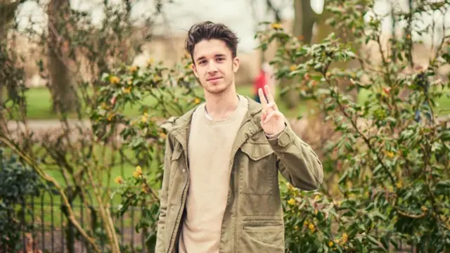 Mikey est debout et fait signe de la main gauche à la caméra