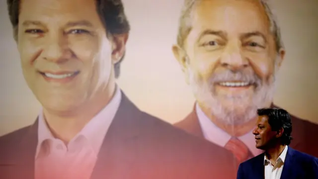 Fernando Haddad no canto interior direito, ao fundo um enorme cartaz com as fotosentrar pixbet saque rápidoHaddad e Lula