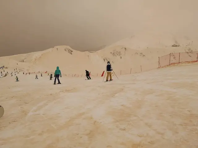 Pessoas esquiam na neve alaranjada