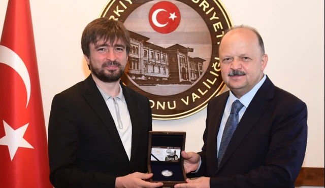 İki adam bir plaketi tutarken fotoğrafçıya poz veriyor