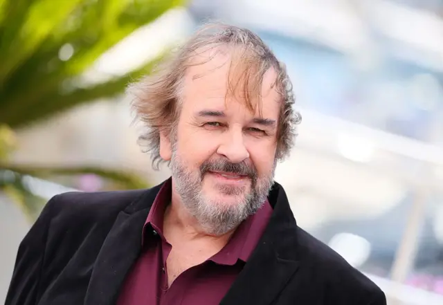 Peter Jackson kırmızı halıda yürürken poz veriyor.