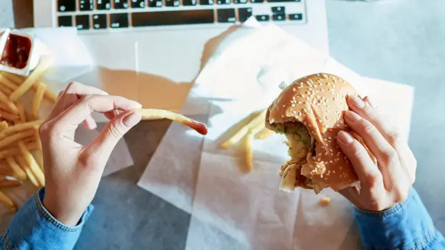 Mulher comendo hambúrguer e batatas fritas