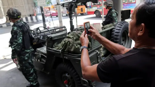Bir kişi cep telefonuyla Taylandlı askerin fotoğrafını çekiyor.