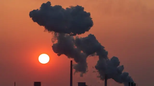 Fumée provenant de cheminées industrielles sur fond de ciel rouge.
