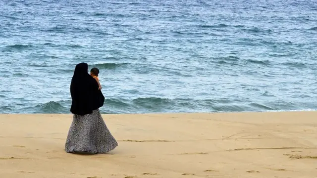 In this picture taken on April 25, 2019, a Sri Lankan Muslim woman walks along a beach with her child in Kattankudy. - Zahran Hashim's sword-wielding zealotry fuelled fears in the sleepy east coast town of Kattankudy long before the cleric became Sri Lanka's most wanted man over the horrific Easter Sunday suicide attacks. The country's president announced on April 26 that Hashim led and died in the attack on the Shangri-La hotel in Colombo -- one of three hotels and three churches hit by bombers wearing explosive backpacks.