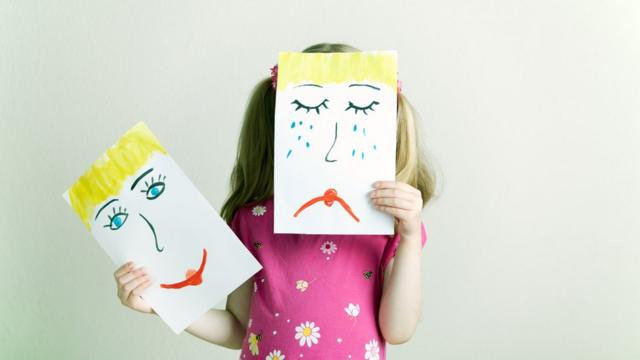 Criança segura desenhos simbolizando tristeza e alegria