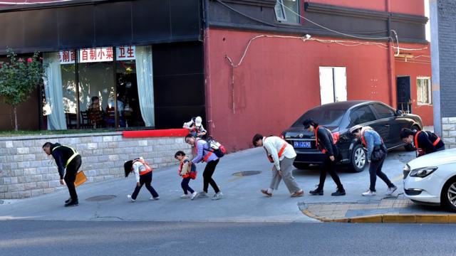 為了躲避攝像頭，鄧玉峰和幾名參與者在幸福大街上彎腰前行。