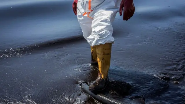 Un travailleur marche dans de l'eau contaminée par du pétrole.