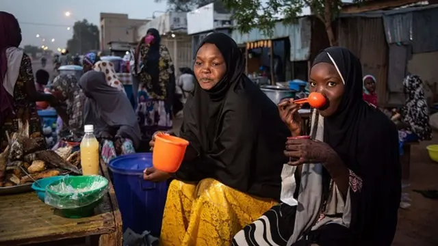 Women prepare to break their fast by drinking millet porridge on the side of the road in the Lazaret district of Niamey on Friday, April 24, 2020 as Muslims prepare to break their fast on the first day of the holy month of Ramadan. - The Iftar took place calmly in Niamey after riots in protest against the curfew and the ban on collective prayers, decreed to fight against the spread of the coronavirus.