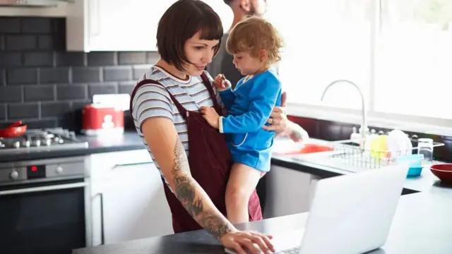 Mãe trabalha na cozinha enquanto segura o filho no colo