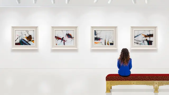 A woman sitting at an art gallery, looking at pictures - we don't know what she's thinking.