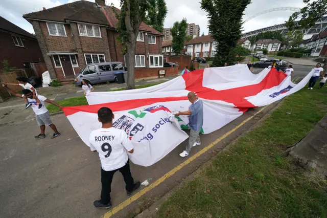 Local residents carry a giant England flag from Neeld Crescent in Brent, where Raheem Sterling grew up, on their way to Wembley Stadium