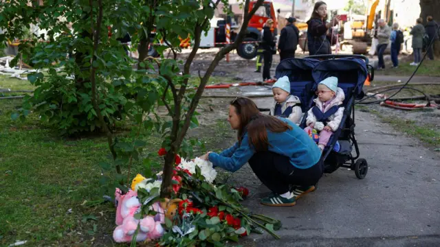 Мајка са двоје деце оставља цвеће у парку за страдале