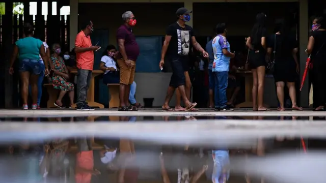 Diversas pessoas de máscara em fila em área externa de construção