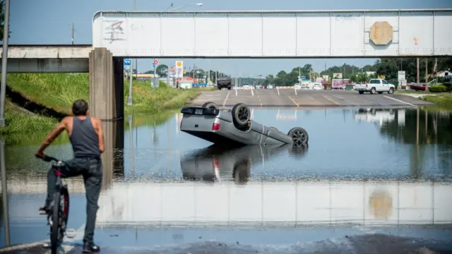 Seorang pria dengan sepedanya memeriksa truk yang terbalik ditengah banjir di Porth Arthur, Texas
