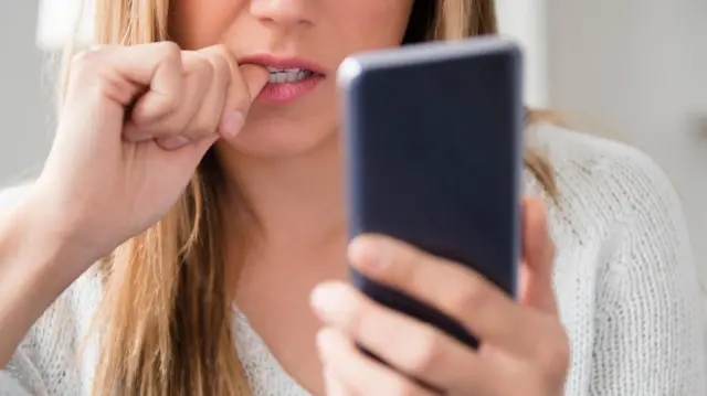 زنی که چهره‌اش کامل پیدا نیست در حال دیدن موبایل