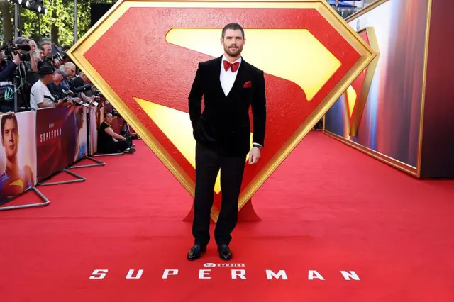 Ator David Corenswet usando terno preto e gravata borboleta vermelha durante lançamento do filme