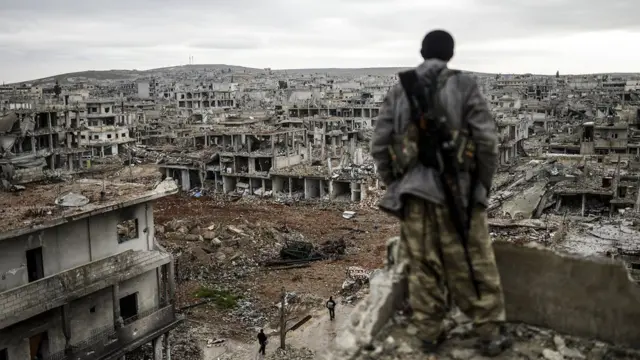 Kürt bir savaşçı harabeye dönmüş Kobani kentine bakıyor.