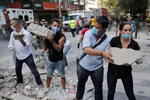 Across Mexico City, group of rescue workers and volunteers use shovel and dia bare hand carry blocks from di broken pieces of buildings wey di earthquake fall.