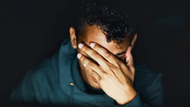 Hombre joven con mano cubriéndose la cara en señal de preocupación.