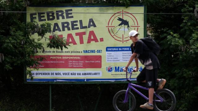 Homem passacef loteria federalfrente a placa que diz 'Febre amarela mata'