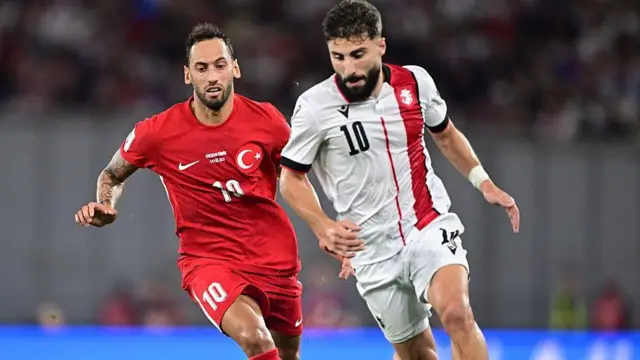 Hakan Çalhanoğlu ve Gürcü bir futbolcu top mücadelesi yapıyor