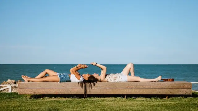 Des filles allongées sur un banc, au bord de la mer, en train d'envoyer des textos.
