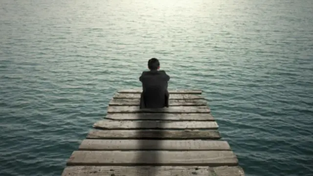 شاب يجلس وحيدا أمام بحيرة للتأمل