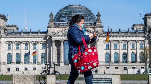 A woman walks past the Reichstag in Berlin in a face mask