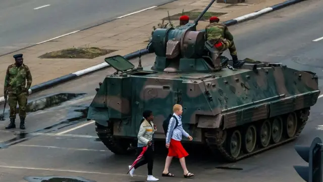 Young women walk past an armoured personnel carrier in the streets of the capital Harare on 15 November 2017
