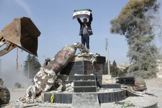 مردی که با پرچم سوریه به جای مجسمه کاوه آهنگر ایستاده است