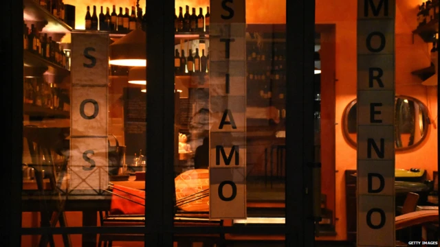 A sign outside a restaurant window in Rome, which says: 'Help! We are dying.'