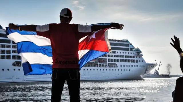 Un hombre sostiene una bandera cubana frente al crucero.