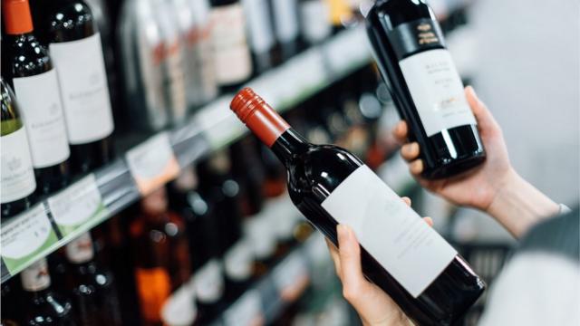 Pessoa segurando duas garrafastvbet onlinevinho tintotvbet onlinefrente a uma prateleiratvbet onlinevinhos no mercado