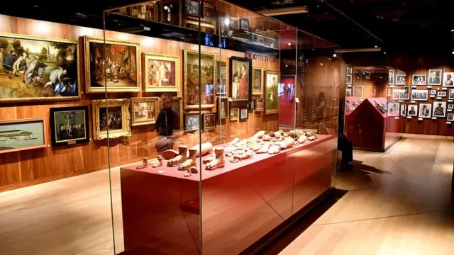 Музейный зал с картинами и фотографиями на стенах и витриной в центре