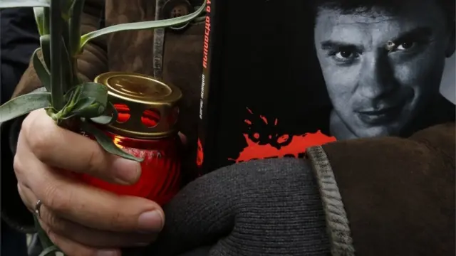 Boris Nemtsov fotoğrafı basılı bir dergi ve mum taşıyan bir Rus