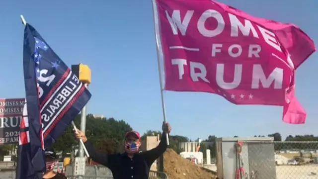 毛里奥挥舞着两面旗，一面蓝色，另一面粉红色是妻子的。