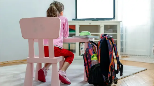 Em casa, menina sentada diantecomo criar aposta na novibetmesa e TV, com mochila ao lado