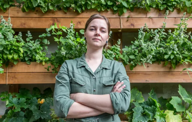 Viktoria Mosina, chef at Grun Cafe, standing in front of her allotment mounted on the wall of the restaurant