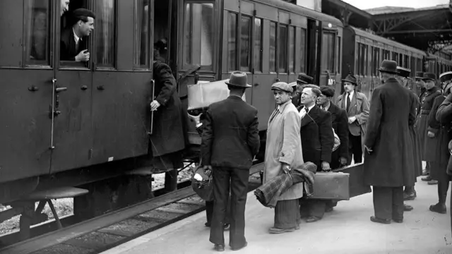 Imagem mostra estaçãobets bola bets bolatrem, com homens parados na plataforma, embarcando ou já no interior do veículo, olhando pela janela