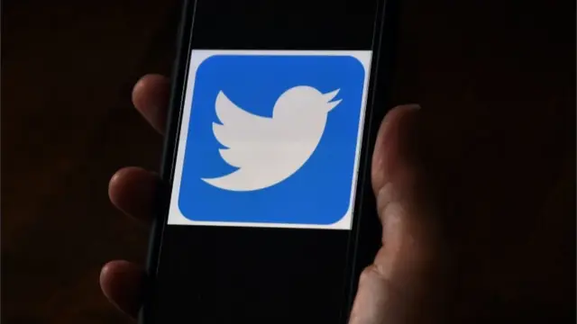 Tangan menggenggam ponsel yang layarnya menunjukkan logo Twitter.