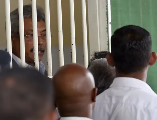 Sri Lanka's former defence ministry chief Gotabhaya Rajapaksa (L), the brother of the former strongman leader Mahinda Rajapaksa, looks on from a court detention cell at the magistrate court in Colombo on September 30, 2016. Gotabhata and six others were granted bail following corruption charges made against them by the anti-graft commission over an alleged illegal operation over a floating armoury.