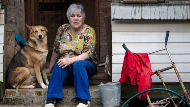 Mulher idosa sentada na porta de casa, com um cachorro