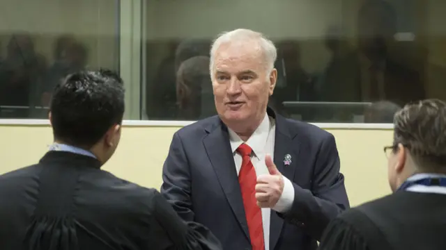 Ratko Mladic dando un apretón de manos a sus abogados defensores antes del inicio de la audiencia